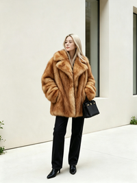 Full-length view of a blonde woman posing in a honey amber oversized faux fur coat with a black handbag.