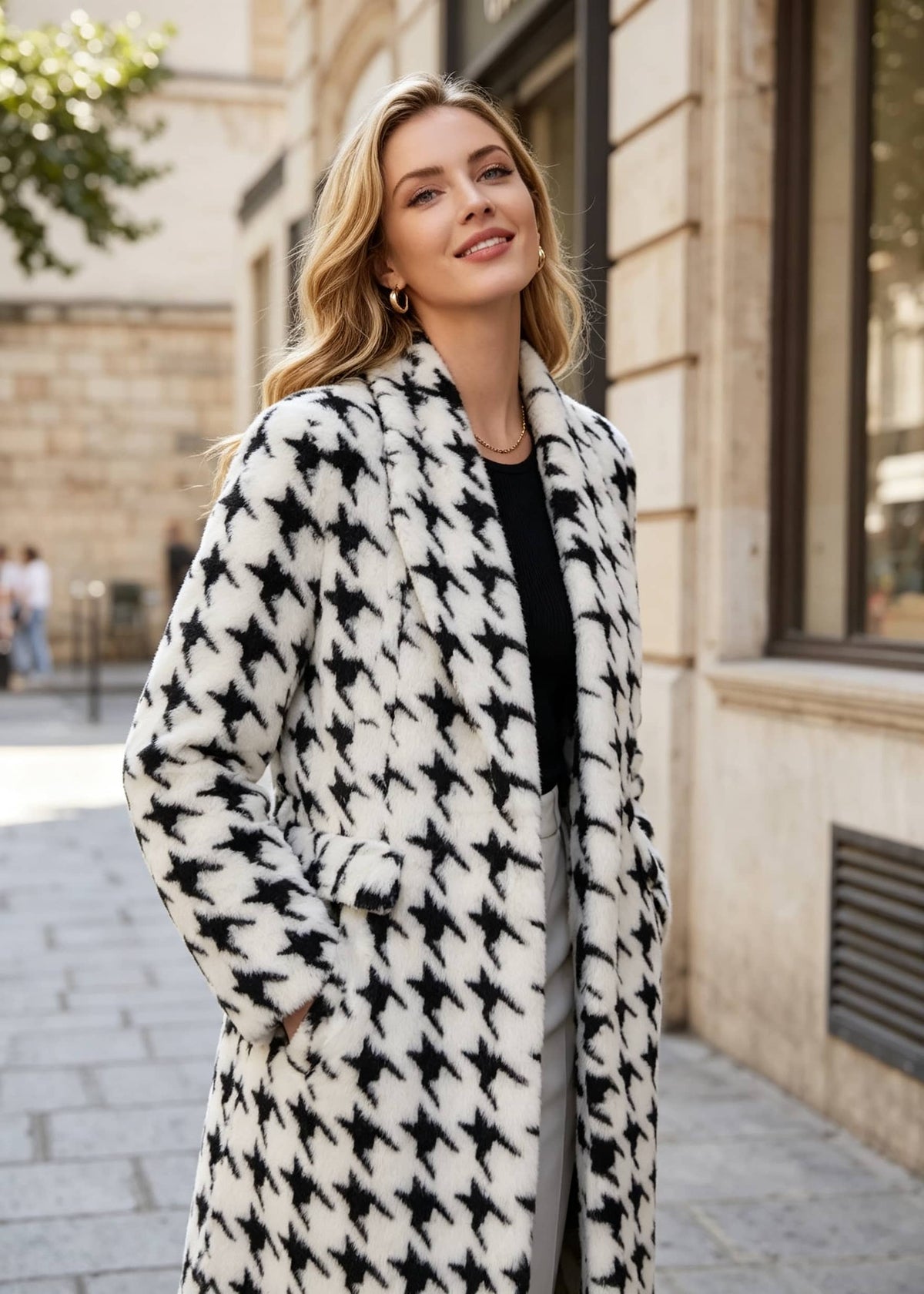 A woman wearing a black and white houndstooth patterned coat over a black top, standing on a city street.