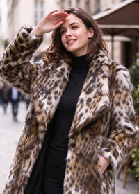 Outdoor candid portrait of a woman shading her eyes while modeling a leopard print spread lapel faux fur midi coat.  
