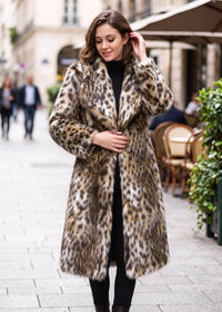 Front-facing full-length street view of a woman wearing the leopard print spread lapel faux fur midi coat touching her collar.  