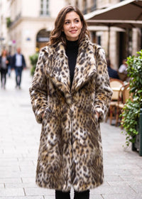 Front three-quarter street shot of a smiling woman with hands in pockets wearing a leopard faux fur midi winter coat.