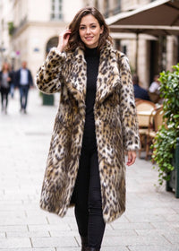 Dynamic full-body walking pose of a smiling woman in a leopard pattern faux fur midi coat strolling down a city street.  