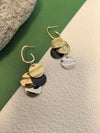 Pair of multi-colored disc dangle earrings displayed on a diagonal backdrop of solid green and textured beige.