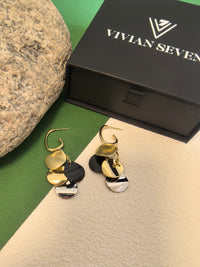 Pair of multi-colored disc dangle earrings on a green and textured beige backdrop, next to a closed black box labeled "VIVIAN SEVEN."