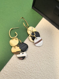 Pair of multi-colored disc dangle earrings on a backdrop of green and textured beige, with one of the silver-effect discs featuring a brown/black stripe design.