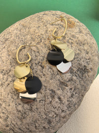 Pair of dangle earrings with multiple round, multi-colored disks resting on a large, rough grey stone.