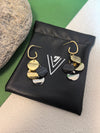 Pair of multi-colored disc dangle earrings resting on a small black pouch with a white "V" logo, next to a grey stone.