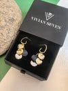 Pair of multi-colored disc dangle earrings presented in an open black gift box labeled "VIVIAN SEVEN" on a textured surface next to a grey stone.