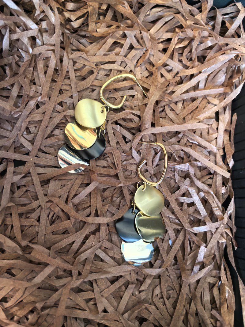 Pair of multi-colored disc dangle earrings lying on a bed of shredded brown paper packaging.