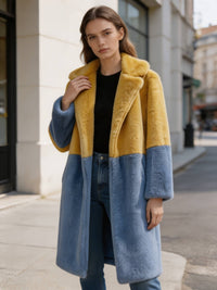 Woman wearing a mustard yellow and slate blue block long faux fur coat paired with a black top and denim pants.