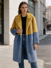 Front view of a woman wearing a lapel-collar mustard and slate blue two-tone plush faux fur long coat outdoor.
