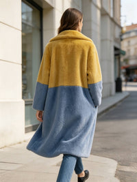 Back view of a woman walking in a long mustard yellow top and slate blue bottom two-tone faux fur winter coat.