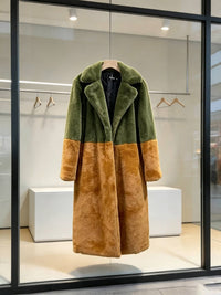 Olive green and rust brown colorblock faux fur long coat displayed on a wooden hanger in a store window.