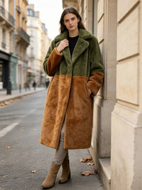 Model leaning against a building wall wearing an olive and rust brown colorblock faux fur long coat with hand in pocket.