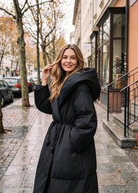 Vivian Seven black oversized hooded down coat with wide collar and self-tie belt, smiling pose