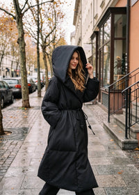 Side angle of Vivian Seven long black wrap puffer coat with dramatic hood and waist tie