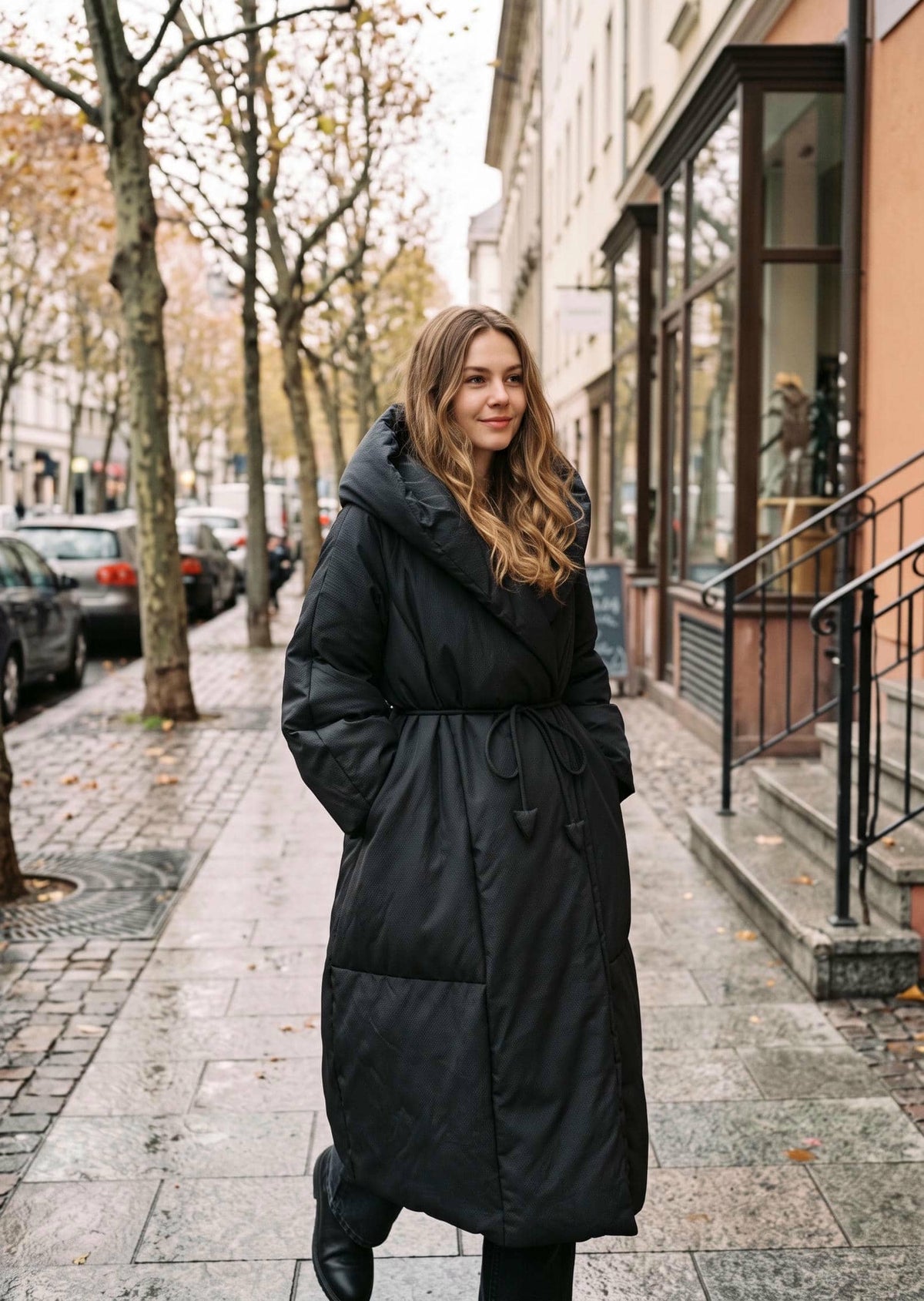 Vivian Seven black wrap down maxi coat with wide shawl collar and hood down, walking pose