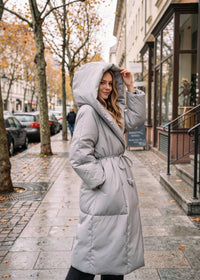 Vivian Seven light gray down puffer coat showing oversized cozy hood and tied waist belt