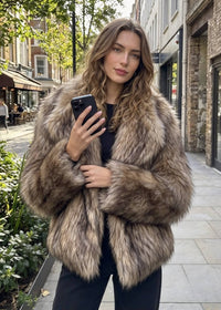 Outdoor street portrait of a woman holding a smartphone while wearing the shaggy tipped faux fur wide-collar jacket.  