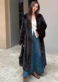 A full-length front view of the woman in the black faux fur coat and denim maxi skirt. The glossy, high-shine texture of the dark fur is emphasized against the neutral urban background.