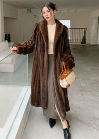 A standing shot of the woman in the brown coat, resting one hand on a glass partition. The coat's vertical fur texture and long silhouette are clearly visible.