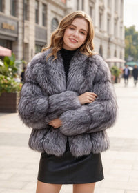 A woman wearing a voluminous gray faux fur jacket over a black top and black mini skirt, standing on a city street.