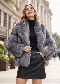 Outdoor three-quarter street shot of a smiling blonde woman holding her lapels in a silver fox frosted faux fur cropped jacket paired with a black leather mini skirt.  