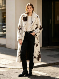 Woman wearing a long spotted faux fur coat, white top, and black jeans standing on a city street.
