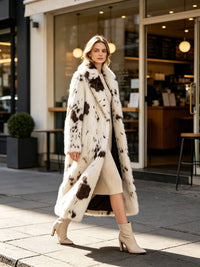 Model walking outside a cafe in an open cow print faux fur long coat, beige dress, and ankle boots.