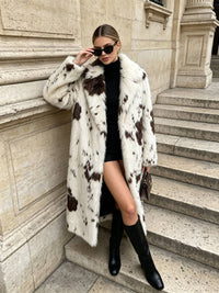 Woman posing on outdoor stone stairs wearing a statement spotted faux fur coat, sunglasses, and knee-high boots.