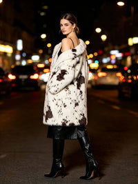 Night view of a woman looking over her shoulder wearing a luxury spotted faux fur coat and high-heeled boots.