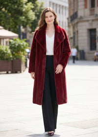 A woman stands on a city sidewalk wearing a long, plush burgundy faux-fur coat over a white top and black wide-leg pants.