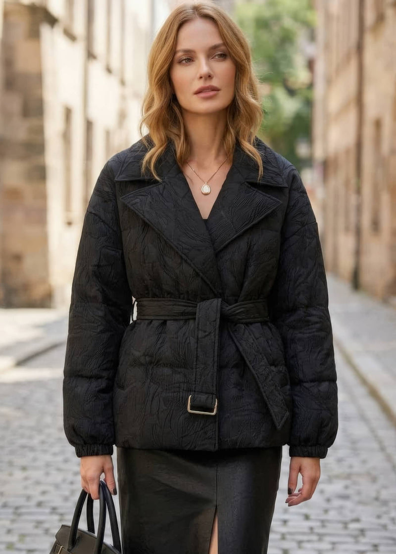 Front view of woman wearing black textured jacquard goose down coat with lapel collar and belted waist