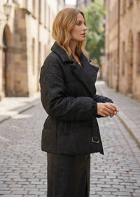 Side profile of woman wearing black textured jacquard down jacket with lapels and elastic cuffs