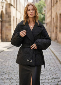 Woman holding lapel of black textured jacquard goose down jacket with belted waist