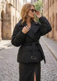 Woman in sunglasses wearing black textured jacquard goose down coat with wide lapels and belt