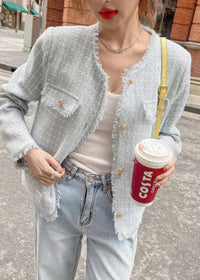 A close-up shot focusing on the details of a light blue-gray tweed jacket with prominent frayed edges and gold buttons. The person wearing it holds a red coffee cup and wears light-wash jeans.
