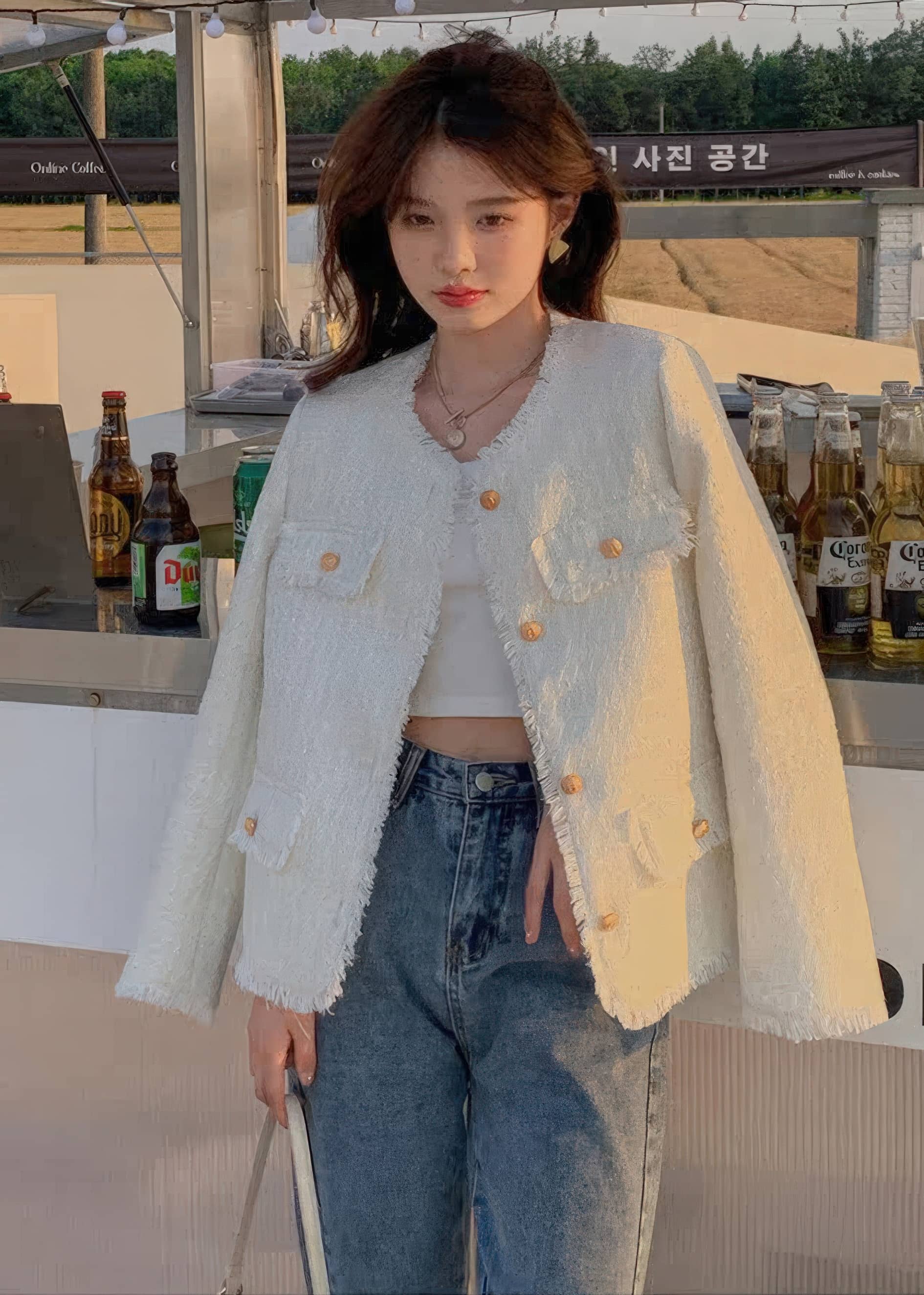 A close-up shot focusing on the details of a light blue-gray tweed jacket with prominent frayed edges and gold buttons. The person wearing it holds a red coffee cup and wears light-wash jeans.