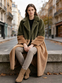 Woman seated on a stone ledge wearing an olive green and camel plush colorblock faux fur long coat.