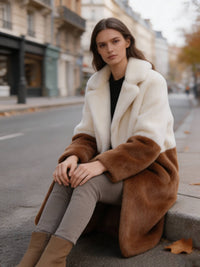 Woman sitting on a curb wearing an off-white and camel colorblock notch lapel faux fur long coat.