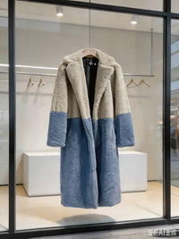 Beige cream and slate blue two-tone notch collar faux fur long coat displayed on a wooden hanger in a boutique window.

