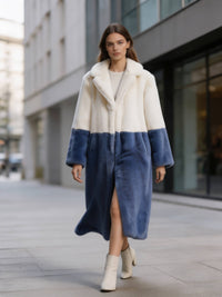 Model walking forward on a city street in a cream white and slate blue two-tone plush faux fur long coat with cream boots.