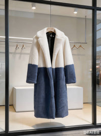 Cream white and slate blue two-tone notch collar faux fur long coat hanging on a hanger in a store window display.