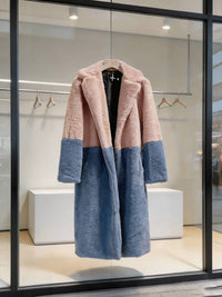 Dusty pink and slate blue color-block notch collar long faux fur winter coat hanging in a modern store display.