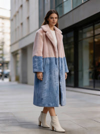 Front pose of a woman wearing a dusty pink and slate blue color-block notch collar faux fur long coat on the street.