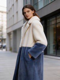 Side view of a model in a cream and slate blue two-tone notch collar faux fur long coat with hand in pocket.
