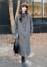 Front view of a woman wearing a buttoned-up houndstooth coat with a high collar and a brown newsboy cap.