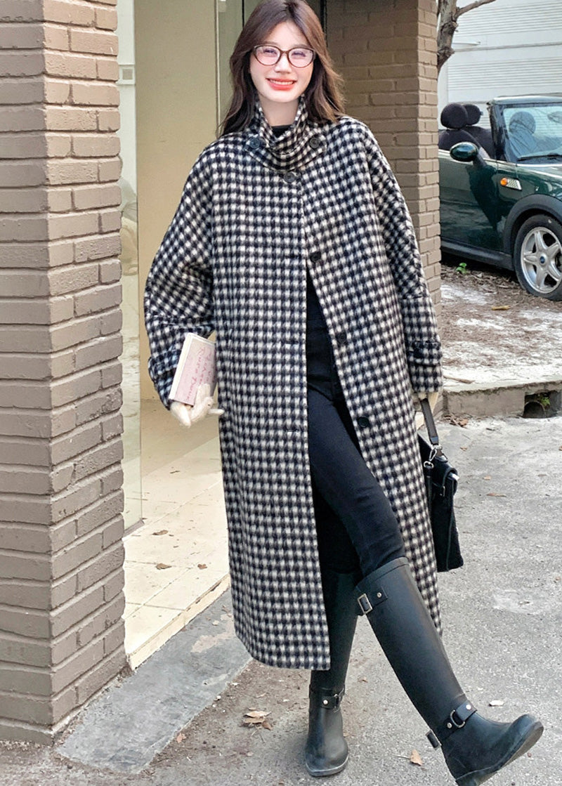 A woman wearing glasses and a long houndstooth coat with one leg forward, showing off tall black buckle boots.
