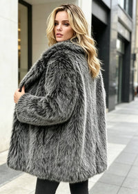 Back three-quarter angle of a blonde woman outdoors showcasing the cut and texture of a salt-and-pepper faux fur coat.
