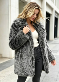 Mid-stride shot of a woman outdoors wearing a grey-and-black faux fur spread collar coat over a white top and dark jeans.